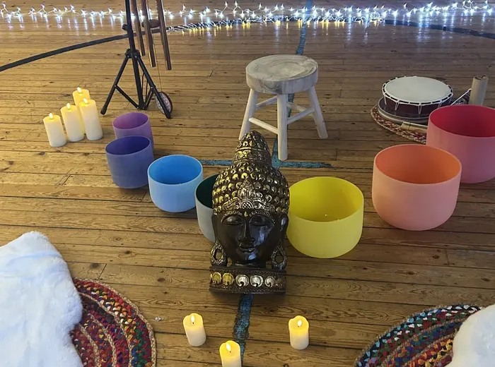 Sound bath setting with coloured bowls, candles and soft furnishings
