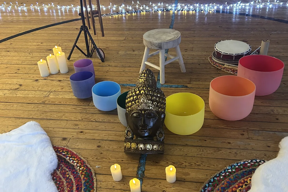 Sound bath setting with coloured bowls, candles and soft furnishings